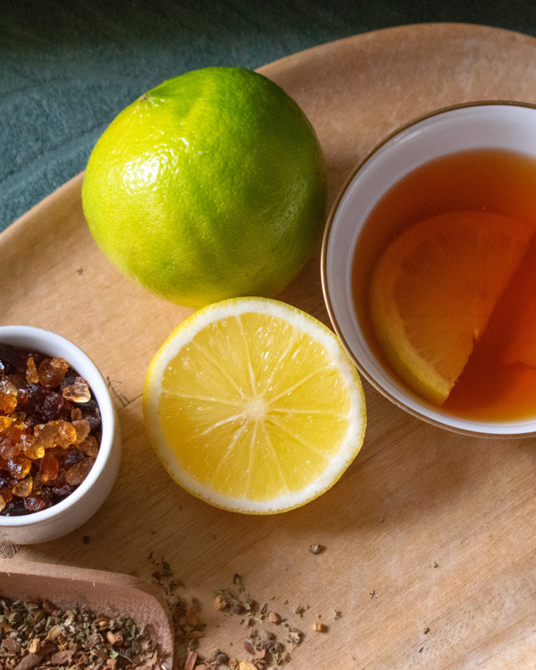 KI generiert: Tee mit Zitronenscheibe, einer Limette, Gewürzen und Kandiszucker auf einem Holztablett.