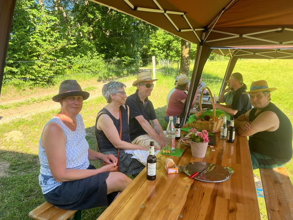 KI generiert: Menschen sitzen an einem Tisch im Freien unter einem Zelt und genießen eine Mahlzeit oder Getränke.