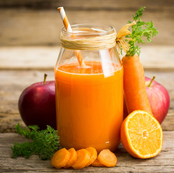 KI generiert: Ein Glas Karottensaft mit Karotten, Apfel und Orange auf einem Holztisch.