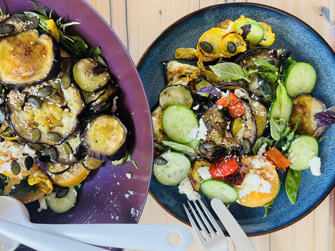 KI generiert: Gemüse-Salat mit Auberginen, Gurken, Kürbiskernen und Feta auf bunten Tellern.