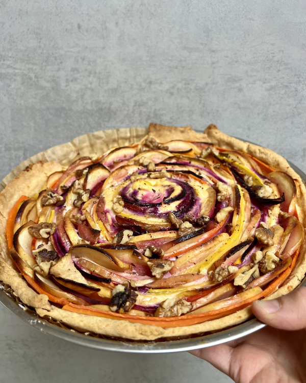 KI generiert: Bunter Gemüsekuchen mit spiralförmig angeordnetem Gemüse auf einem Mürbeteigboden, garniert mit Nüssen.