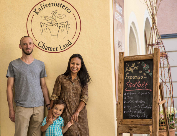KI generiert: Eine Familie vor der Kaffeerösterei Chamer Land. Text: "Kaffee, Espresso, Vielfalt, Zubehör..."