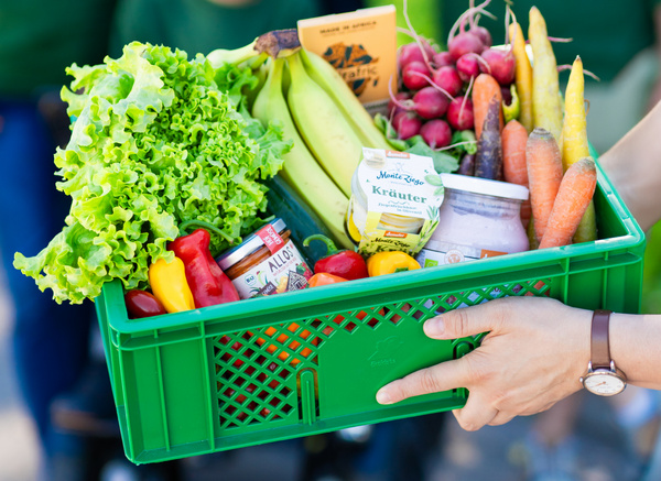 KI generiert: Grüne Kiste mit frischem Gemüse, Obst und Lebensmitteln, darunter Salat, Bananen, Radieschen und Joghurts.