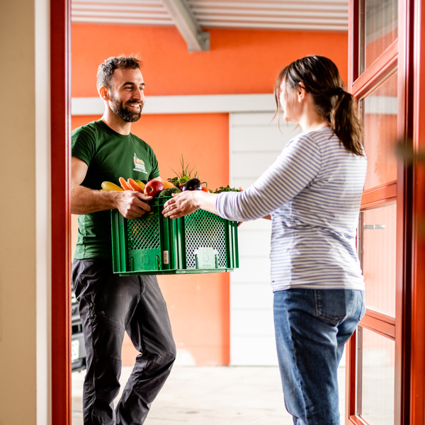 KI generiert: Ein Mann liefert eine Kiste mit Obst und Gemüse an eine Frau an der Tür.