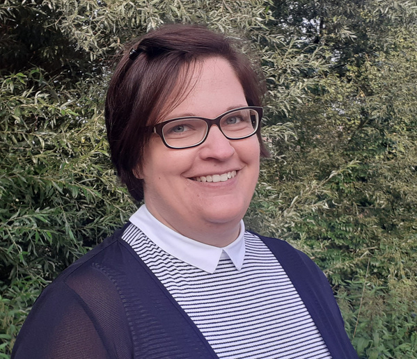 KI generiert: Eine Frau lächelt in die Kamera, umgeben von grünen Bäumen im Hintergrund.