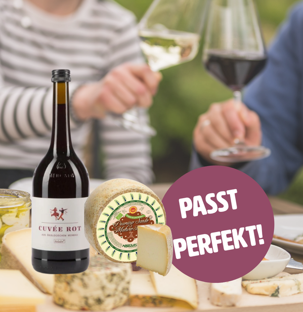 KI generiert: Käse und Wein mit dem Text "PASST PERFEKT!" im Vordergrund, Hände mit Weingläsern im Hintergrund.