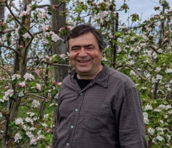 KI generiert: Ein Mann steht lächelnd vor blühenden Bäumen im Freien.