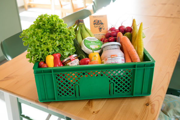 KI generiert: Eine grüne Kiste mit frischem Obst, Gemüse und Bio-Produkten auf einem Holztisch.