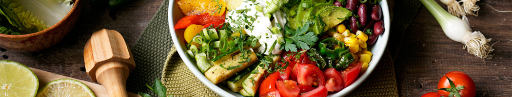 KI generiert: Ein bunter Salat mit Avocado, Tomaten, Bohnen und Mais in einer Schüssel, umgeben von frischem Gemüse und Limetten.