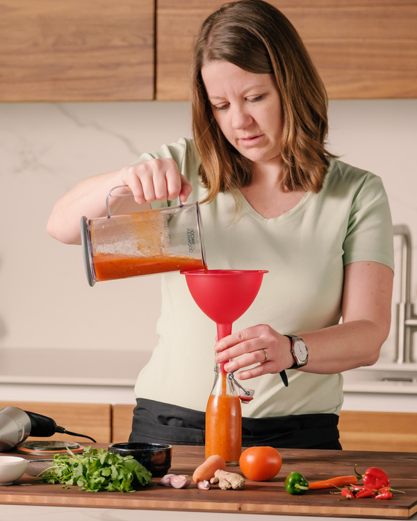 KI generiert: Eine Frau füllt mit einem Trichter eine Flasche mit Tomatensauce auf.