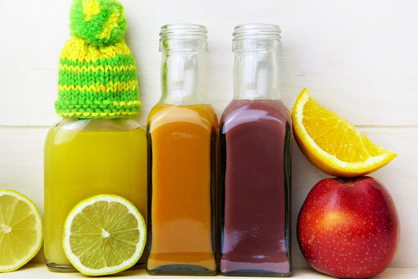 KI generiert: Drei bunte Saftflaschen mit Früchten; eine Flasche trägt eine gestrickte Mütze.