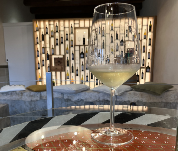 KI generiert: Ein halbvolles Weinglas in einem stilvollen Raum mit beleuchtetem Weinregal im Hintergrund.