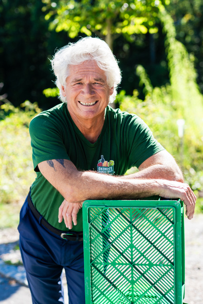 KI generiert: Ein Mann in grünem Shirt lehnt sich auf eine grüne Kiste im Freien. Shirt-Text: "Ökokiste".