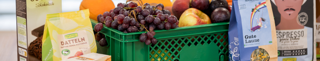 KI generiert: Eine Kiste mit Obst, Datteln, Tee und Kaffee. Text: "DATTELN", "Gute Laune".