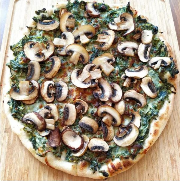 KI generiert: Pizza mit Spinat und Champignons auf einem Holzbrett.