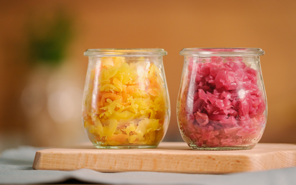 KI generiert: Zwei Gläser mit gelbem und rotem Sauerkraut auf einem Holzbrett.
