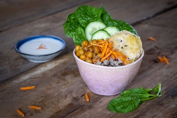 KI generiert: Eine bunte Buddha Bowl mit Quinoa, Kichererbsen, Karotten und Salat. Im Hintergrund steht eine Schale mit Soße.