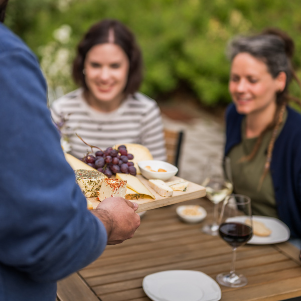 KI generiert: Ein Tisch mit Menschen beim Essen; jemand serviert eine Käseplatte mit Weintrauben.