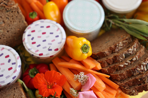 KI generiert: Gemüse, Brotscheiben, bunte Paprika, Karottensticks und Blumen dekorieren ein Picknick.