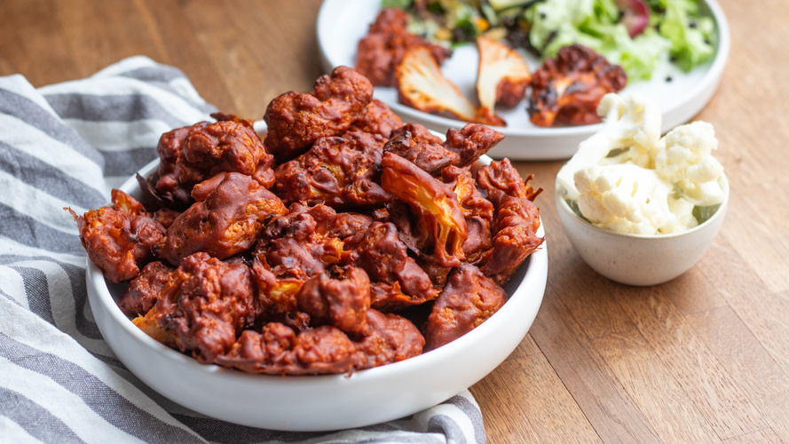 KI generiert: Eine Schüssel mit gebratenen Blumenkohl-Wings, dazu Dip und Salat im Hintergrund.