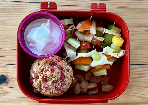 KI generiert: Lunchbox mit Joghurt, einem Muffin, vegetarischen Spießen und Mandeln.