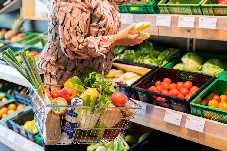 KI generiert: Person beim Einkaufen von Gemüse mit einem Korb voller frischer Produkte im Supermarkt.