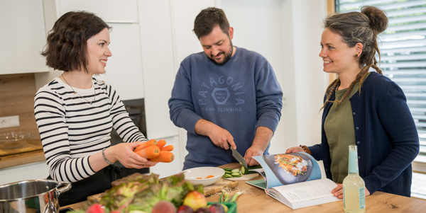 KI generiert: Drei Personen kochen gemeinsam in einer Küche und schneiden Gemüse.