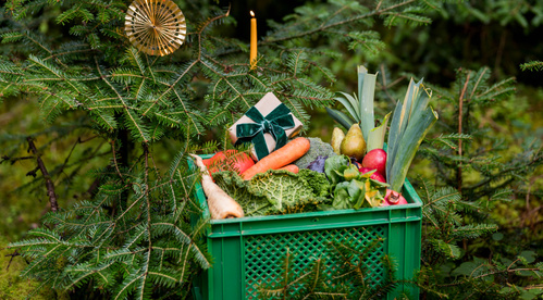 KI generiert: Grüne Kiste mit Gemüse und Geschenkpäckchen in einem Tannenbaum dekoriert.