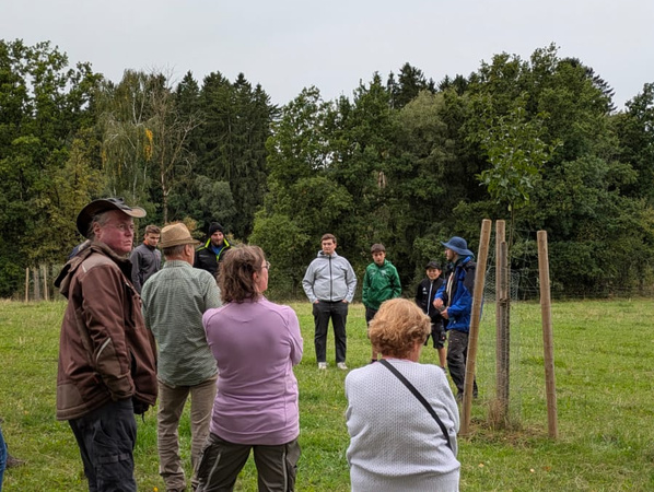 KI generiert: Menschen stehen auf einer Wiese im Kreis und schauen einem Redner zu. Im Hintergrund sind Bäume zu sehen.