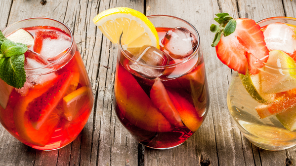 KI generiert: Drei bunte Fruchtcocktails mit Zitronen, Erdbeeren und Eis auf einem Holztisch.