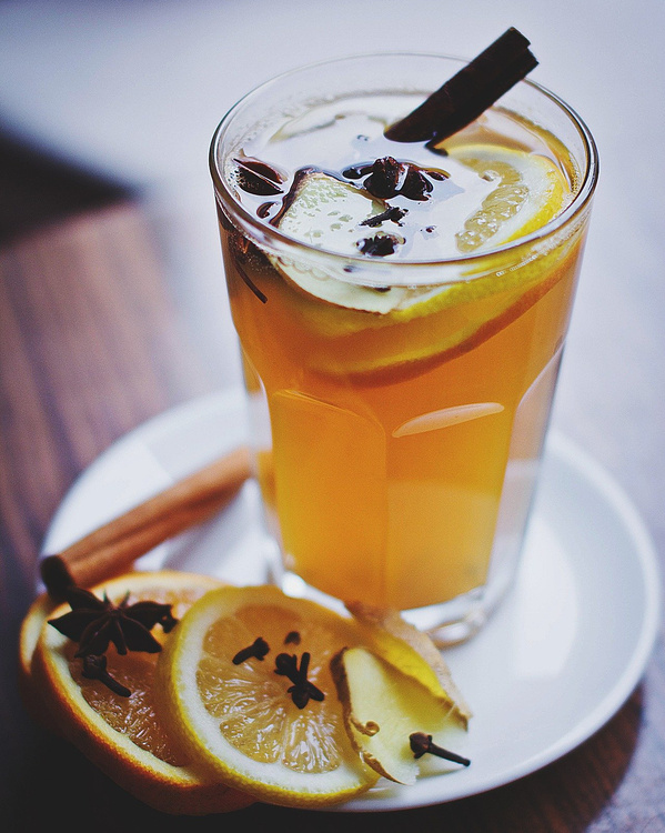 KI generiert: Ein Glas heißen Tee mit Zitrone, Gewürzen und Zimtstange auf einem Teller.
