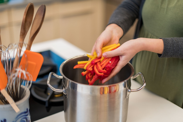 KI generiert: Person füllt geschnittene Paprika in einen Kochtopf in einer Küche.