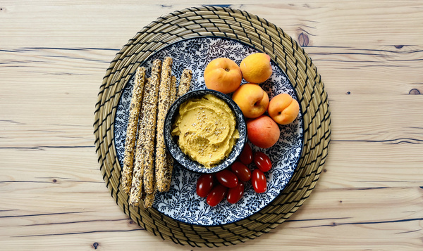 KI generiert: Ein dekorativ arrangierter Teller mit Grissini, Hummus, Cherrytomaten und Aprikosen auf Holzuntergrund.