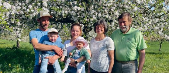 KI generiert: Eine Familie steht lächelnd vor einem blühenden Baum in einer grünen Wiese.
