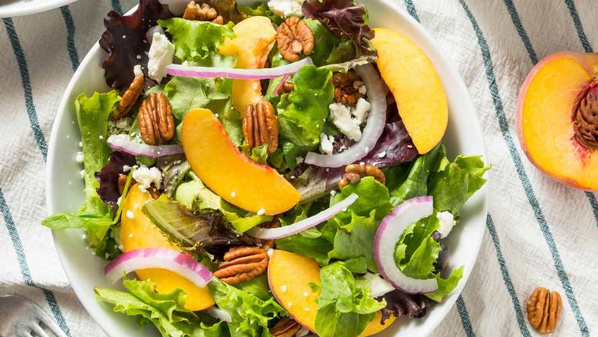 KI generiert: Ein Salat mit Pfirsichen, Pecannüssen, Zwiebeln und Blattsalat in einer Schüssel.