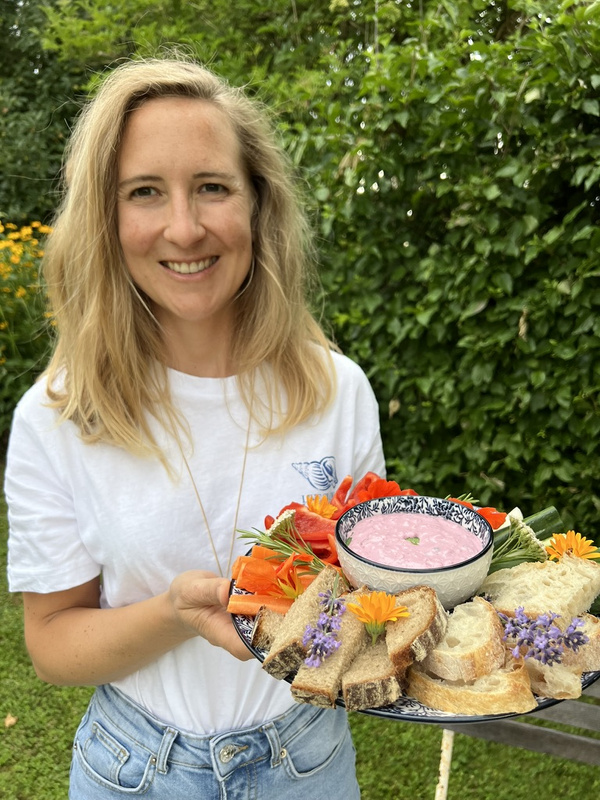 KI generiert: Eine Frau hält ein Tablett mit Brot, Gemüse und Dips vor grünem Hintergrund.
