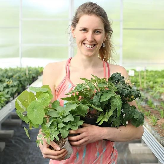 KI generiert: Eine Frau in einem Gewächshaus hält Pflanzen in den Händen.