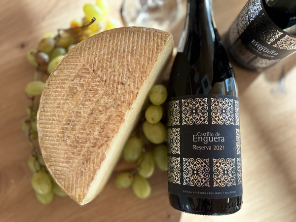 KI-generierte Beschreibung: Hauptinhalt: Brot und Wein auf Holzbrett. Text: "Castillo de Enguera Reserva 2021".