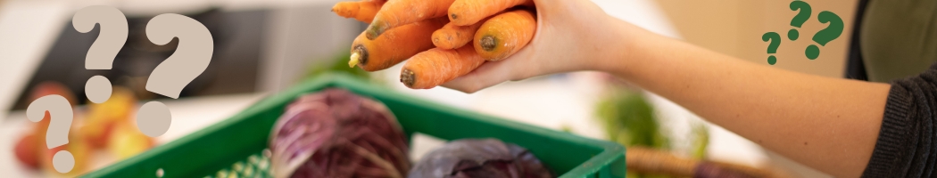 KI generiert: Das Bild zeigt eine Hand, die Karotten hält, während im Vordergrund ein grüner Korb mit weiterem Gemüse, darunter Kohlköpfe, zu sehen ist. Fragezeichen sind im Bild überlagert, was möglicherweise Unsicherheit oder Verwirrung beim Einkaufen symbolisiert.