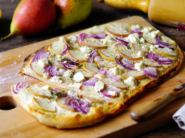 KI generiert: Flammkuchen mit roten Zwiebeln, Birnenscheiben und Käse auf Holzbrett.