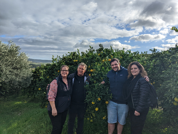KI generiert: Vier Personen stehen vor einem Orangenbaum im Freien, sonniger Himmel.