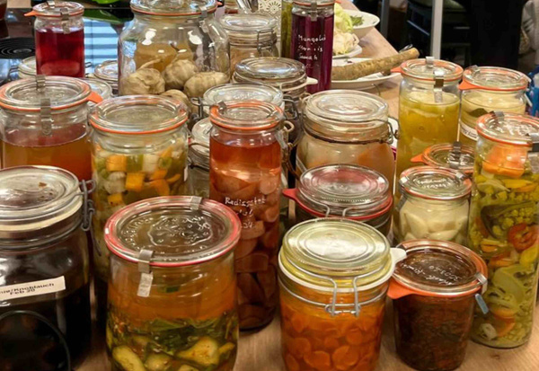 KI generiert: Verschiedene Einmachgläser mit eingelegtem Gemüse und Vorräten auf einem Tisch.