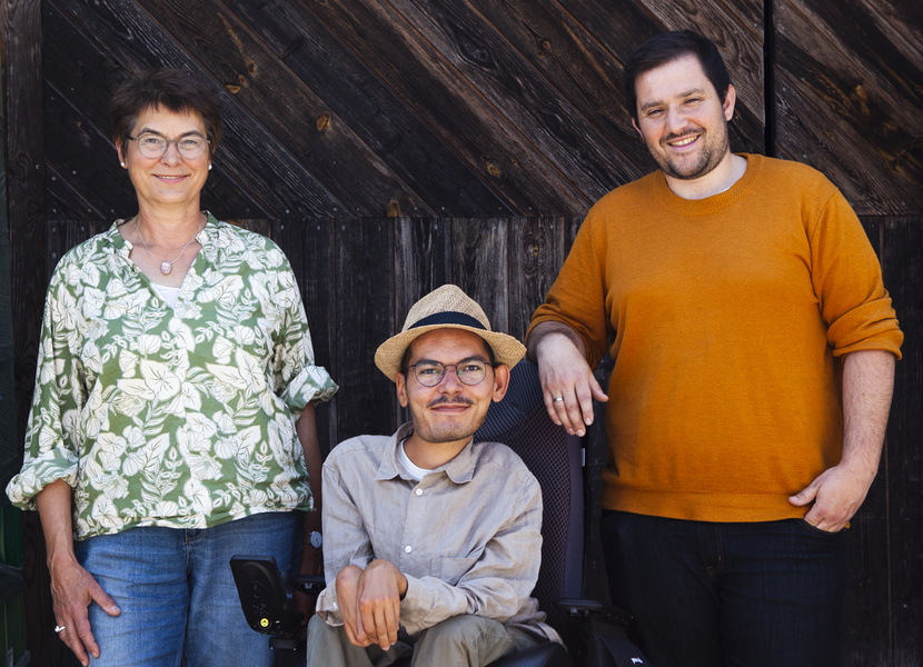 KI generiert: Zwei Personen stehen vor einer Holzwand, die mit verschiedenen Schildern dekoriert ist. Der Mann trägt ein orangefarbenes Oberteil, während die Frau ein gemustertes grünes Hemd trägt.