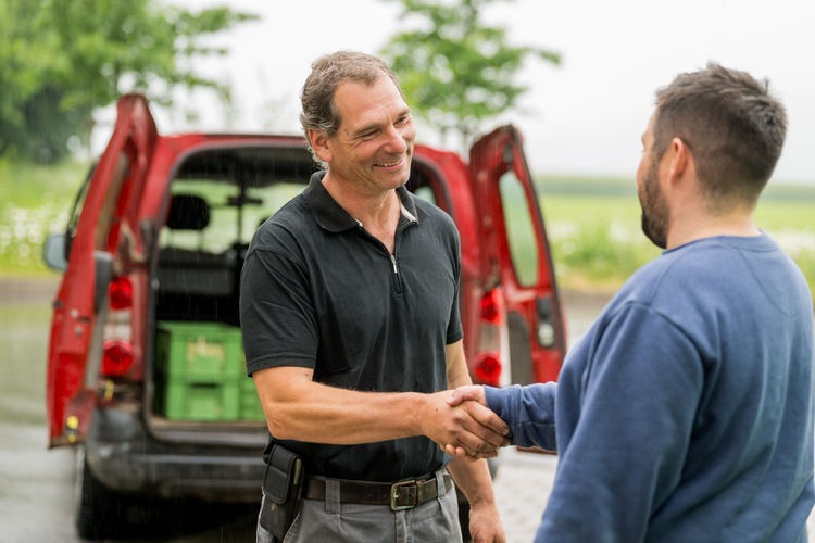 KI generiert: Zwei Männer schütteln sich die Hand vor einem geöffneten Transporter im Freien.