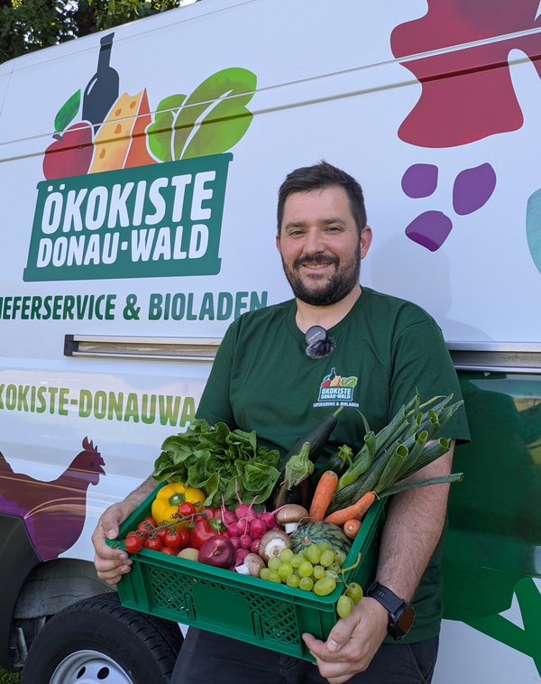 KI generiert: Das Bild zeigt zwei Personen hinter einem Tisch, der mit einer Vielzahl von frischem Obst und Gemüse bedeckt ist. Es gibt ein Werbeschild, das darauf hinweist, dass die sechste Kiste kostenlos ist.