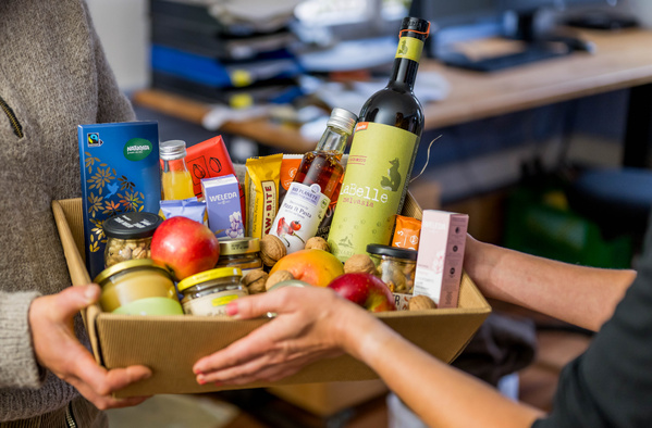 KI generiert: Ein Geschenkkorb mit Lebensmitteln und Getränken, der von zwei Personen gehalten wird.