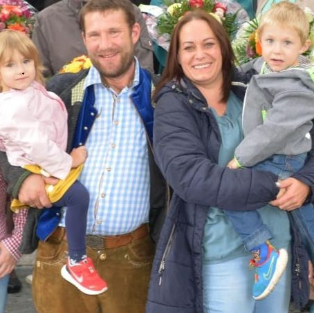 KI generiert: Eine lächelnde Familie mit zwei kleinen Kindern, umgeben von Blumen.