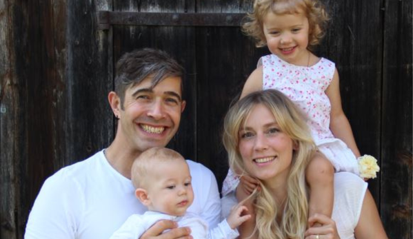 KI generiert: Eine lächelnde Familie mit zwei kleinen Kindern posiert vor einer Holzwand.