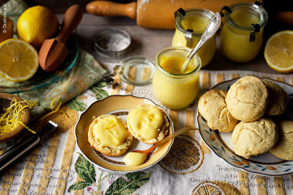 KI generiert: Das Bild zeigt eine appetitliche Anordnung von frisch gebackenem Gebäck mit einer zitronigen Creme, umgeben von Zitronen und weiteren Backutensilien. Der Fokus liegt auf der handgemachten Zitronencreme und den dazugehörigen Brötchen.