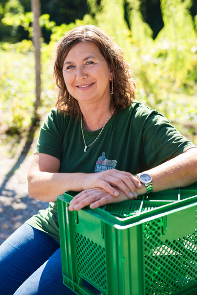 KI generiert: Eine Frau sitzt draußen und lehnt sich auf eine grüne Kiste. Text: "Ökokiste".